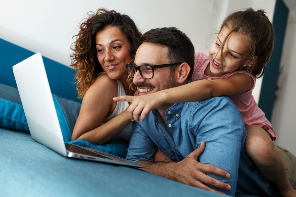 Happy family lies on bed and watching something on laptop